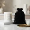 Weiße Kerze im Glas neben einem eleganten schwarzen Samtbeutel auf Marmor.