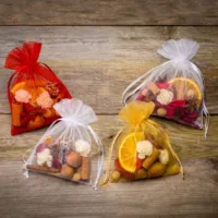 Bunte Organzasäckchen gefüllt mit Potpourri, Zimtstangen und getrockneten Orangenscheiben auf Holz