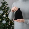 Ein schwarzer Samtbeutel auf der Hand vor einem funkelnden Weihnachtsbaum.