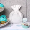 Weißer Geschenkbeutel aus Stoff neben Cupcakes mit "It's a BOY!" Deko für Babypartys.