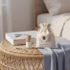Duftsäckchen mit Lavendel-Print und Biene auf einem Rattantisch neben einem Flakon